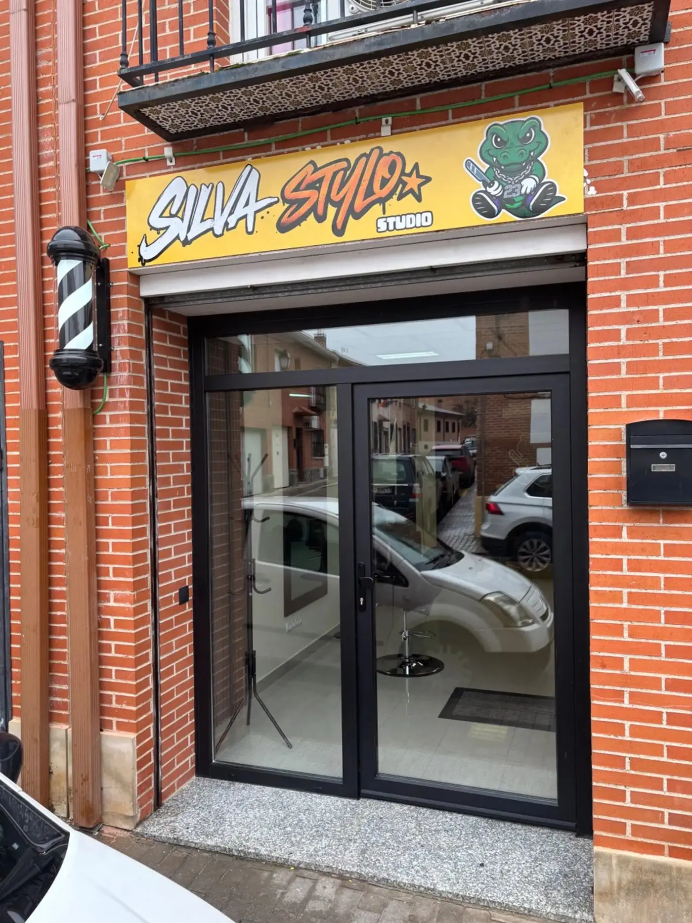Fachada de ladrillo de Silva Stylo Studio con el poste de barbero y el cartel del cocodrilo
